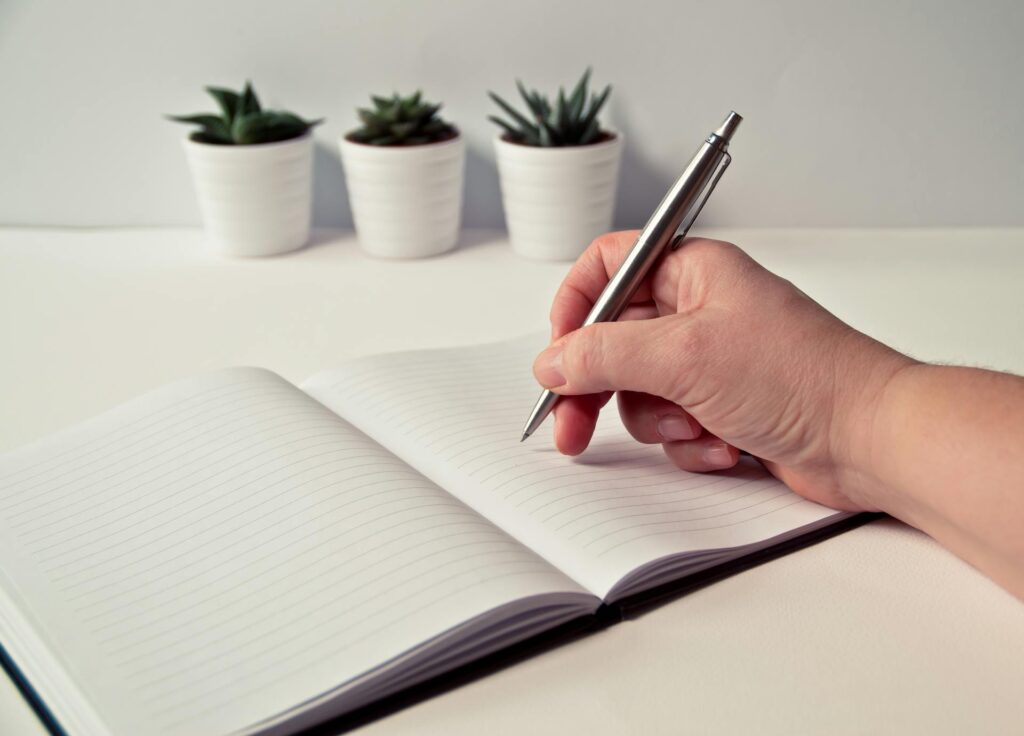 Hands writing in a notebook on a tidy desk, representing the small daily tasks the 2-minute rule clears.